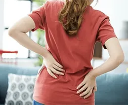 Mulher vestindo uma camiseta vermelha com as duas mãos na coluna sinalizando dor